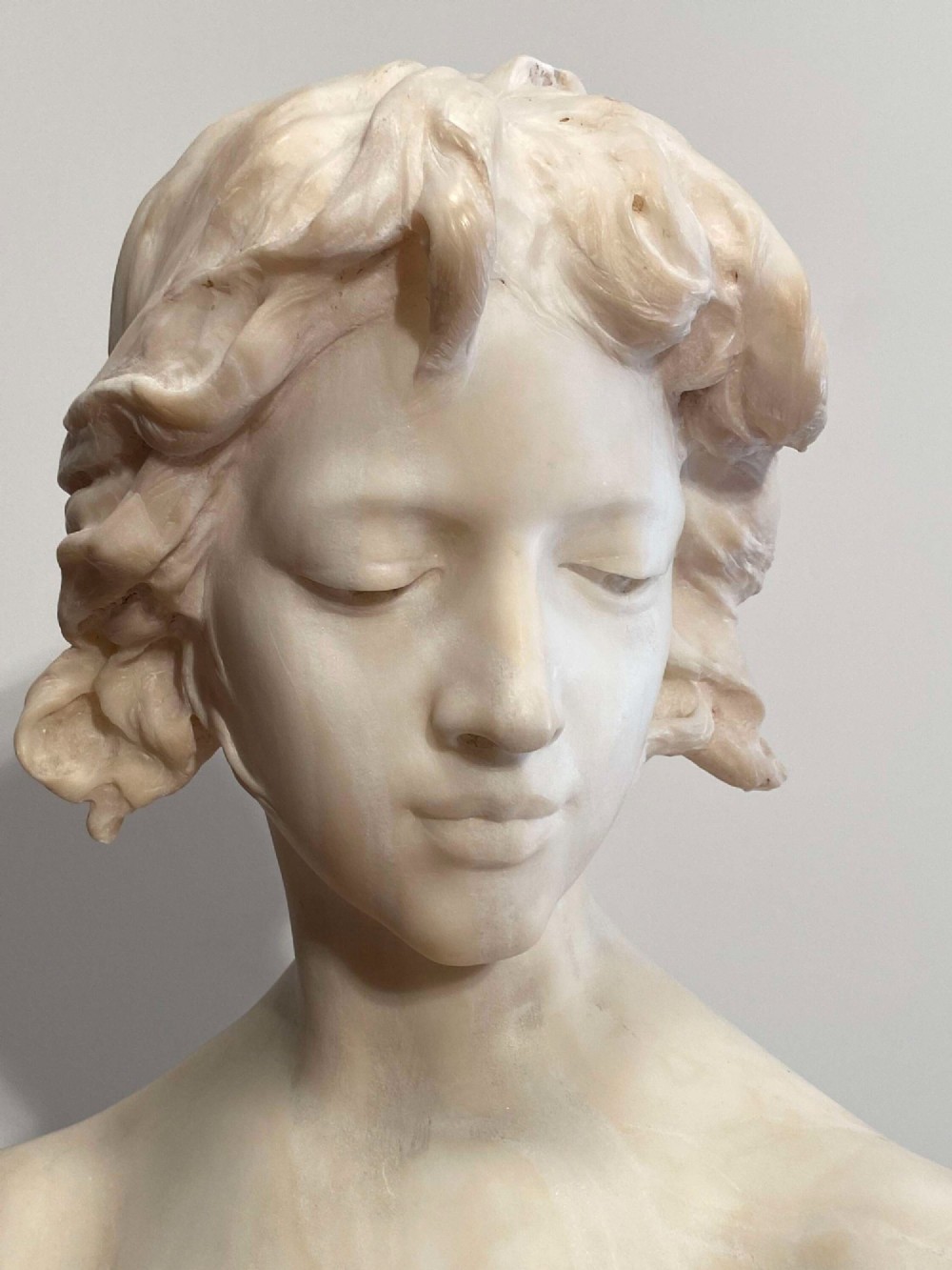 An early twentieth-century carved Carrara marble bust depicting a young female subject with a carved floral corsage, mounted on a wooden pedestal base. View XV