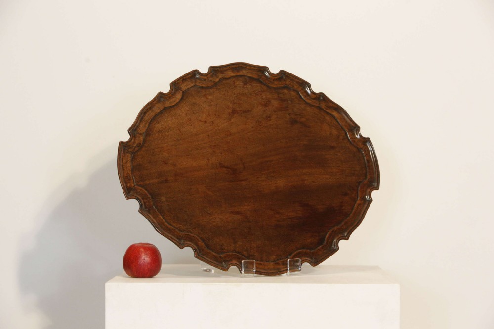 A George III mahogany oval tray featuring a hand-carved pie crust scalloped rim and rich wood grain.