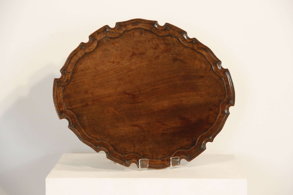 A George III mahogany oval tray featuring a hand-carved pie crust scalloped rim and rich wood grain. View II