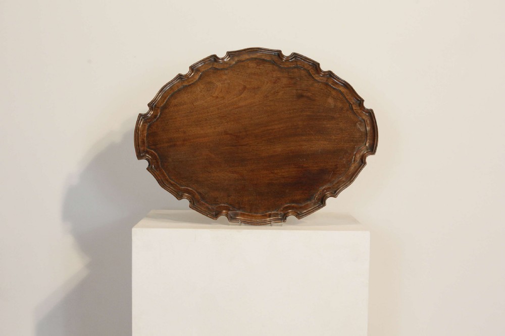 A George III mahogany oval tray featuring a hand-carved pie crust scalloped rim and rich wood grain. View III