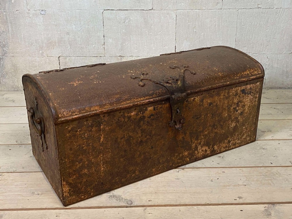An 18th-century wrought iron trunk featuring a domed lid, decorative latch detail, side drop handles, and an oxidised rust brown surface.
