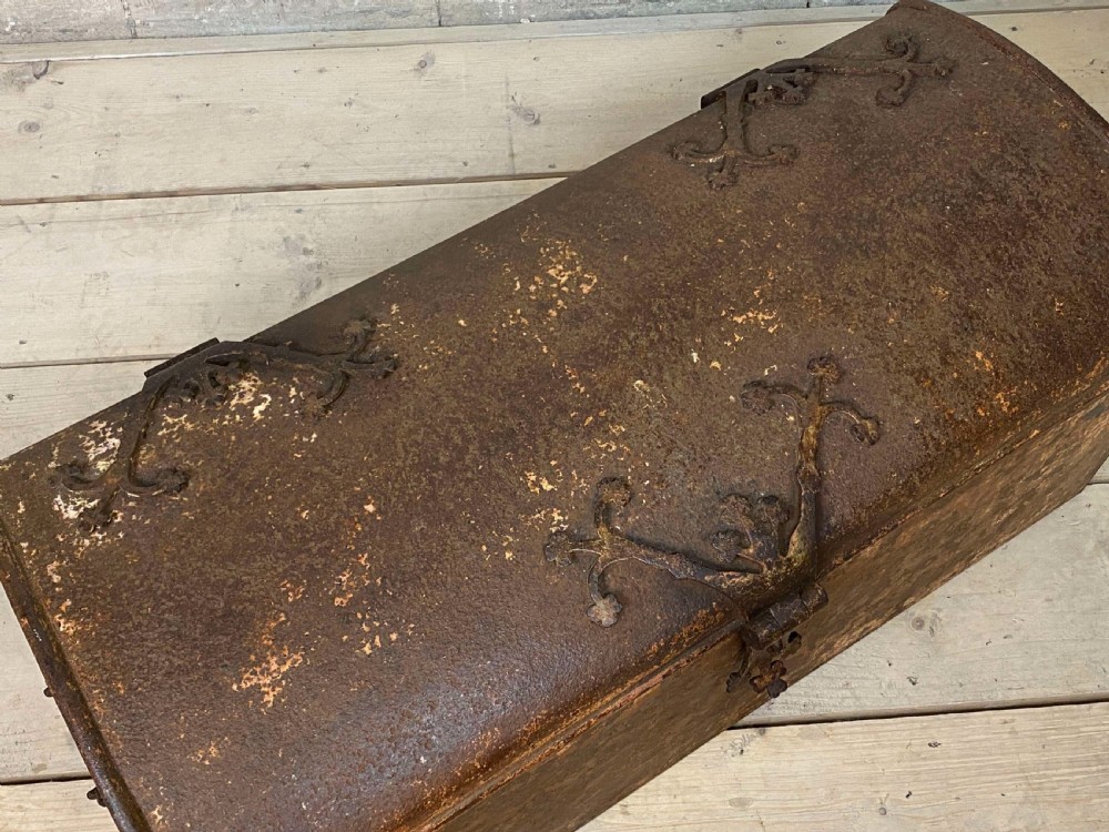 An 18th-century wrought iron trunk featuring a domed lid, decorative latch detail, side drop handles, and an oxidised rust brown surface. View V