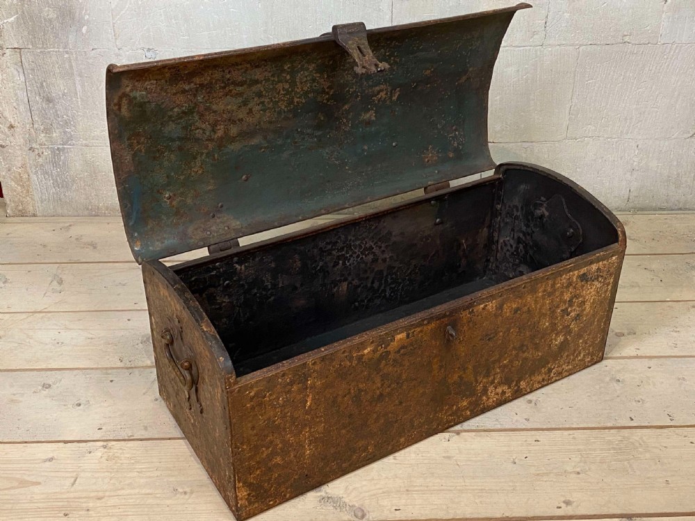 An 18th-century wrought iron trunk featuring a domed lid, decorative latch detail, side drop handles, and an oxidised rust brown surface. View VI