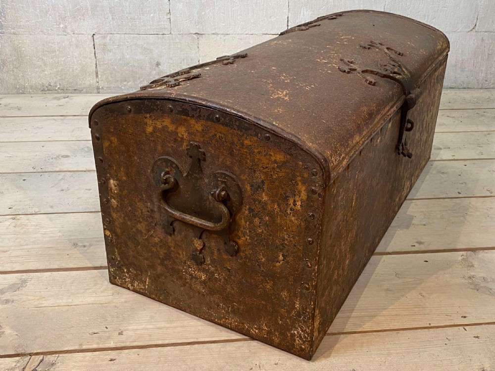An 18th-century wrought iron trunk featuring a domed lid, decorative latch detail, side drop handles, and an oxidised rust brown surface. View VII