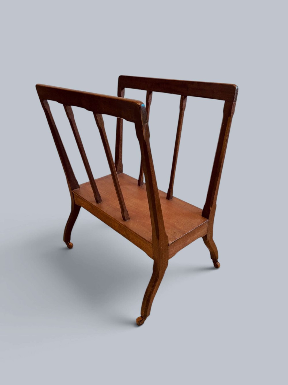A mahogany folio display stand featuring slatted side uprights, a solid lower shelf, and slender legs on brass castors.