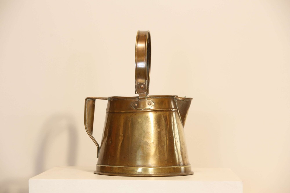 An antique brass hot water can featuring a tapered cylindrical body, broad overhead swinging handle, rear side handle, and riveted construction. View II