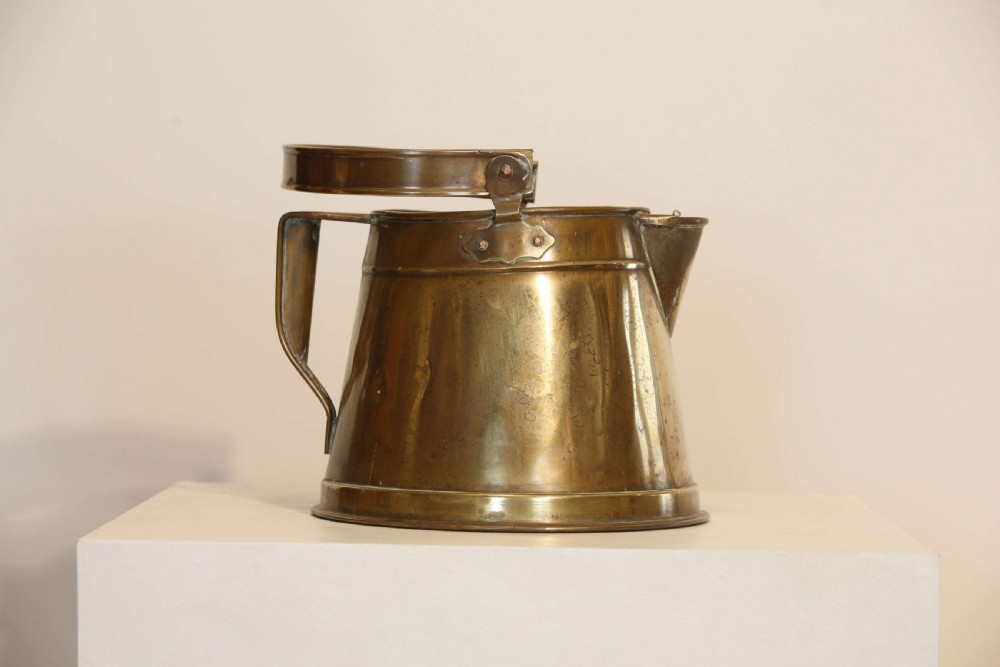 An antique brass hot water can featuring a tapered cylindrical body, broad overhead swinging handle, rear side handle, and riveted construction. View V