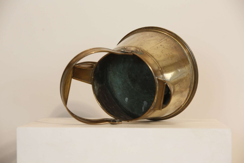 An antique brass hot water can featuring a tapered cylindrical body, broad overhead swinging handle, rear side handle, and riveted construction. View VII
