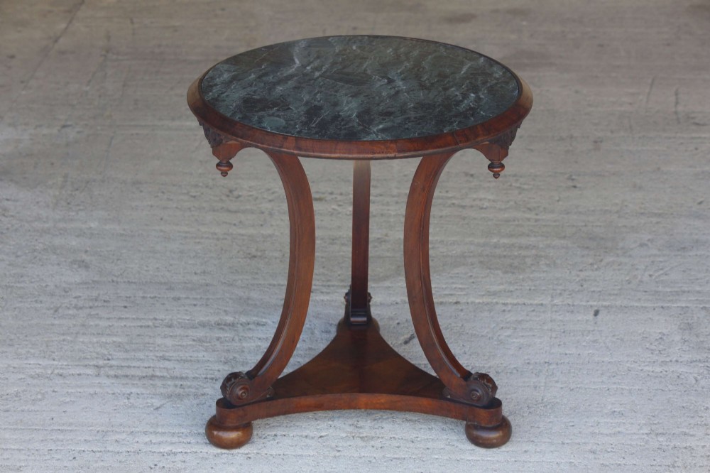 A circular 19th-century French gueridon table featuring a dark green marble top supported by three curved mahogany legs resting on a shaped triform base.