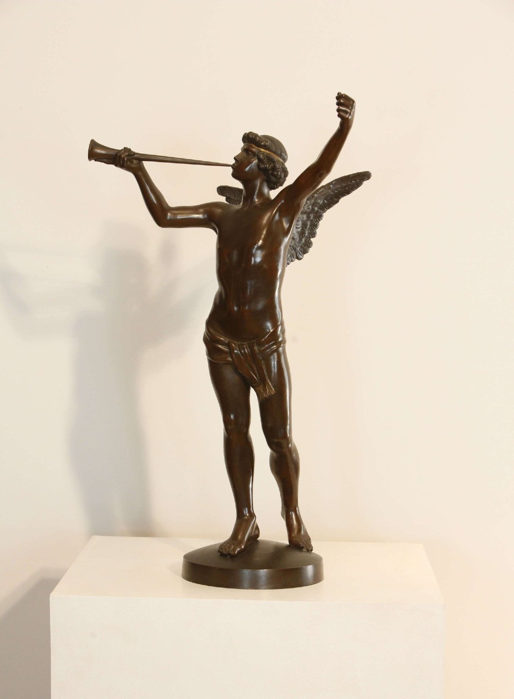A 19th-century dark brown patinated bronze sculpture depicting the winged Archangel Gabriel blowing a trumpet raised on a round base.