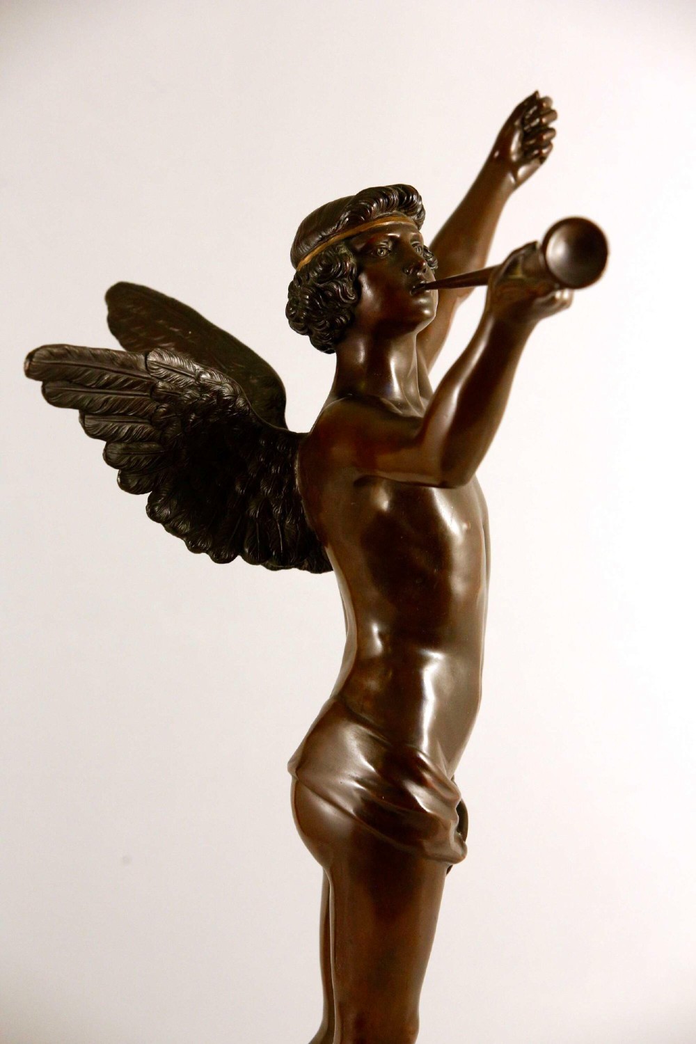 A 19th-century dark brown patinated bronze sculpture depicting the winged Archangel Gabriel blowing a trumpet raised on a round base. View XII