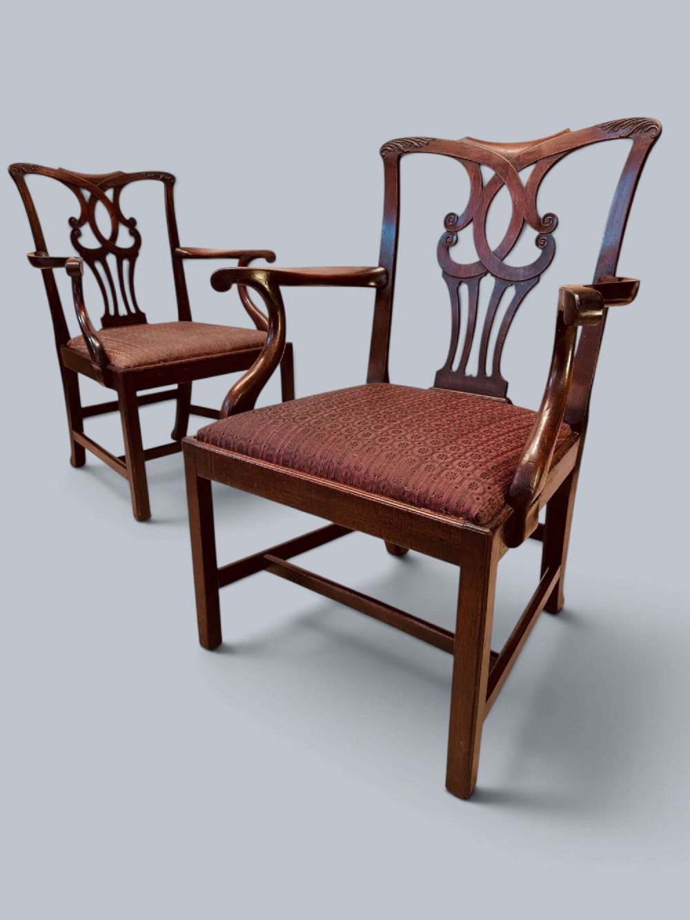 A pair of 19th-century mahogany Chippendale style armchairs featuring carved pierced splat backs, curving armrests, and patterned fabric seats.