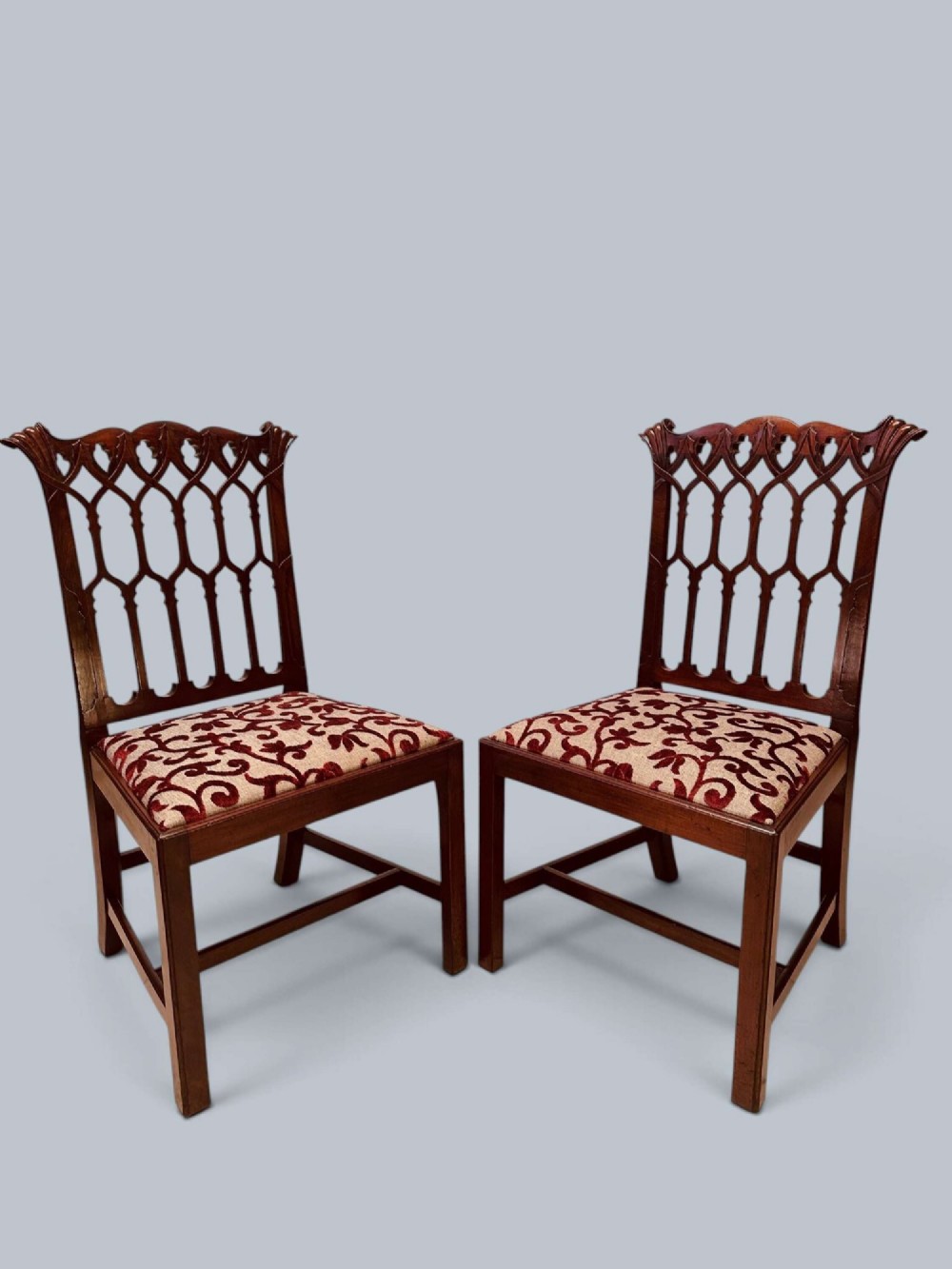 A pair of mahogany side chairs featuring pierced Gothic tracery backrests, straight square legs with H-stretchers, and patterned red fabric upholstery. View II