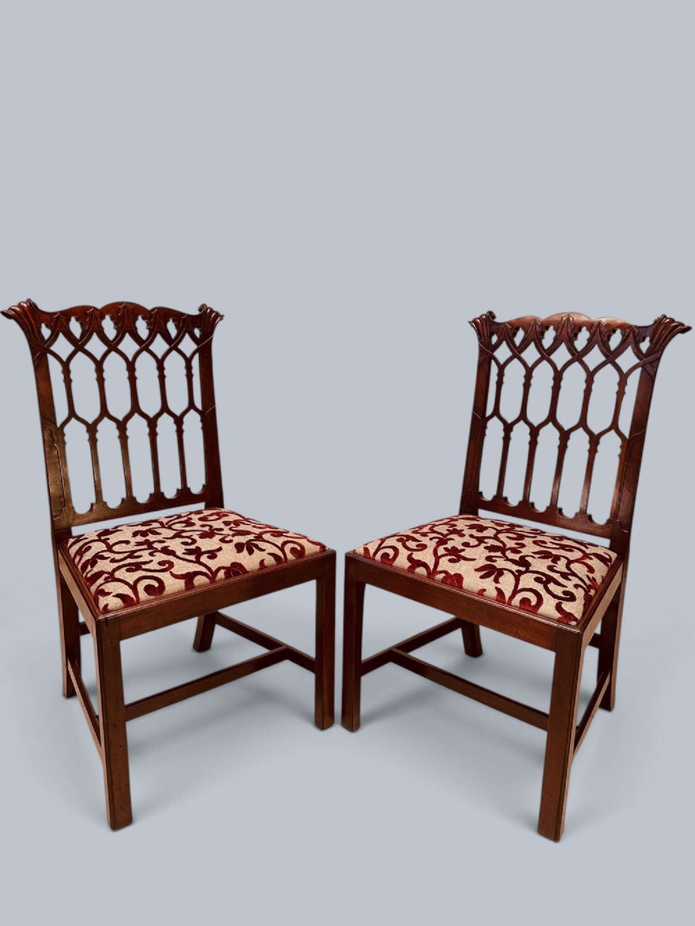 A pair of mahogany side chairs featuring pierced Gothic tracery backrests, straight square legs with H-stretchers, and patterned red fabric upholstery. View IV