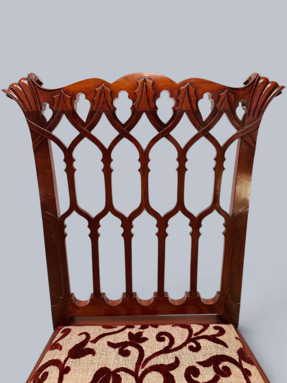 A pair of mahogany side chairs featuring pierced Gothic tracery backrests, straight square legs with H-stretchers, and patterned red fabric upholstery. View V