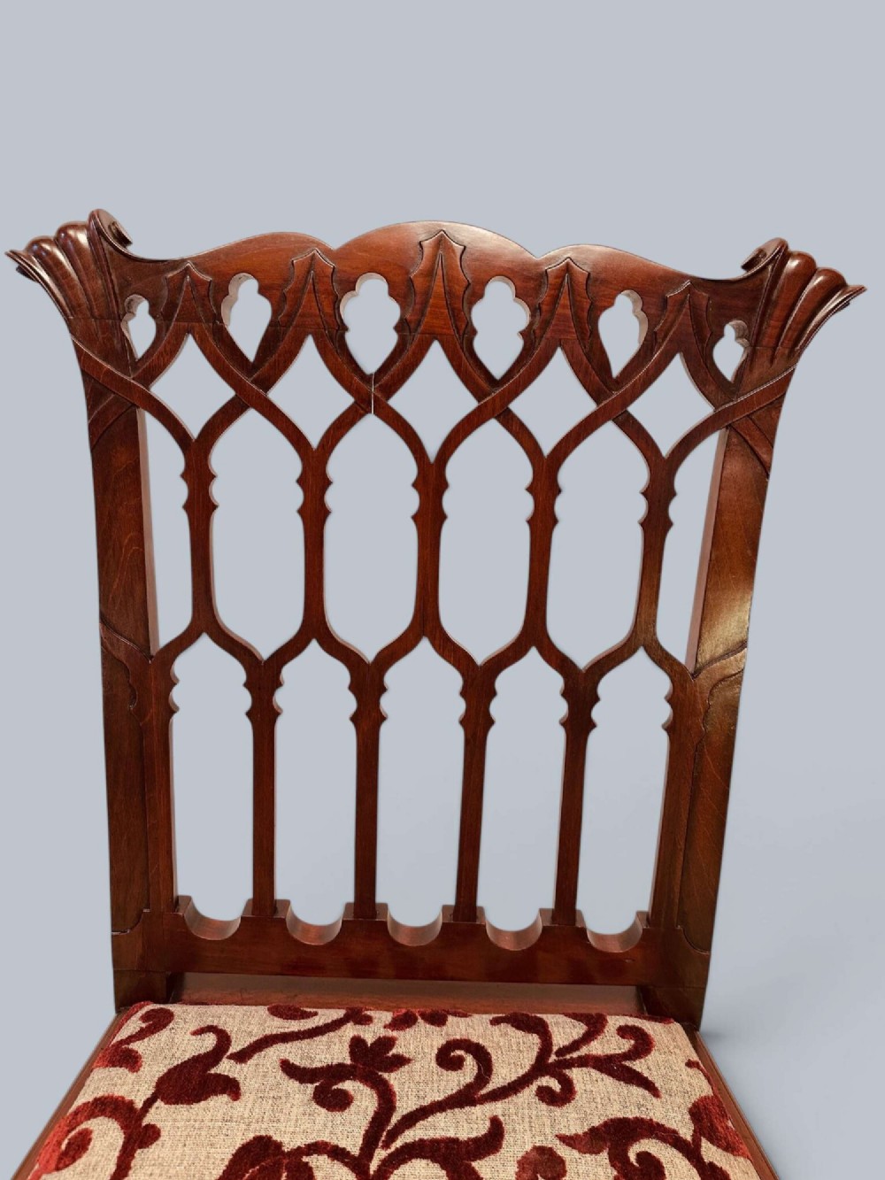 A pair of mahogany side chairs featuring pierced Gothic tracery backrests, straight square legs with H-stretchers, and patterned red fabric upholstery. View VI