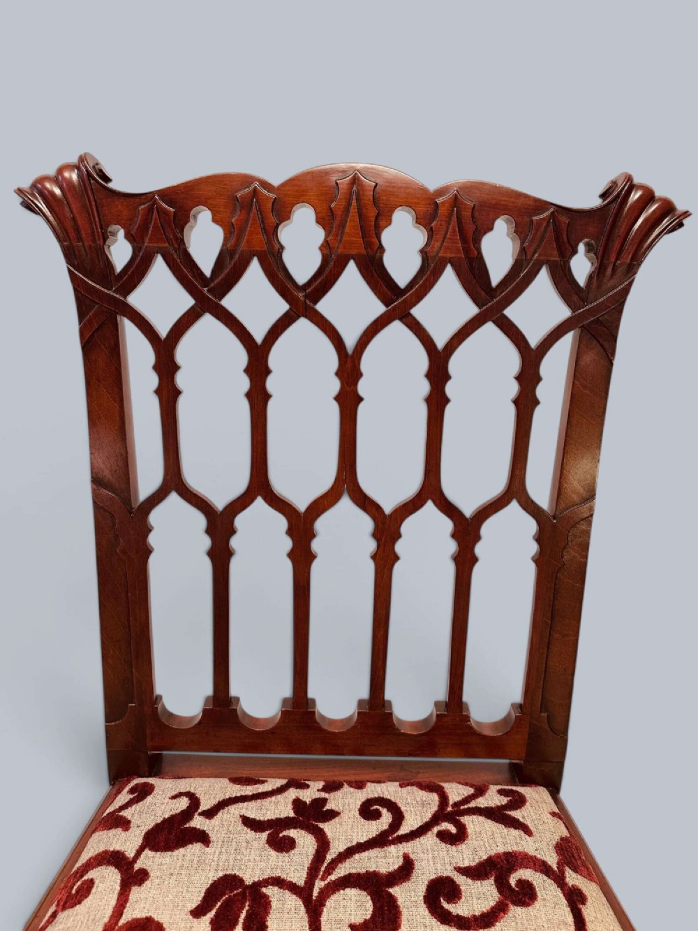 A pair of mahogany side chairs featuring pierced Gothic tracery backrests, straight square legs with H-stretchers, and patterned red fabric upholstery. View VII
