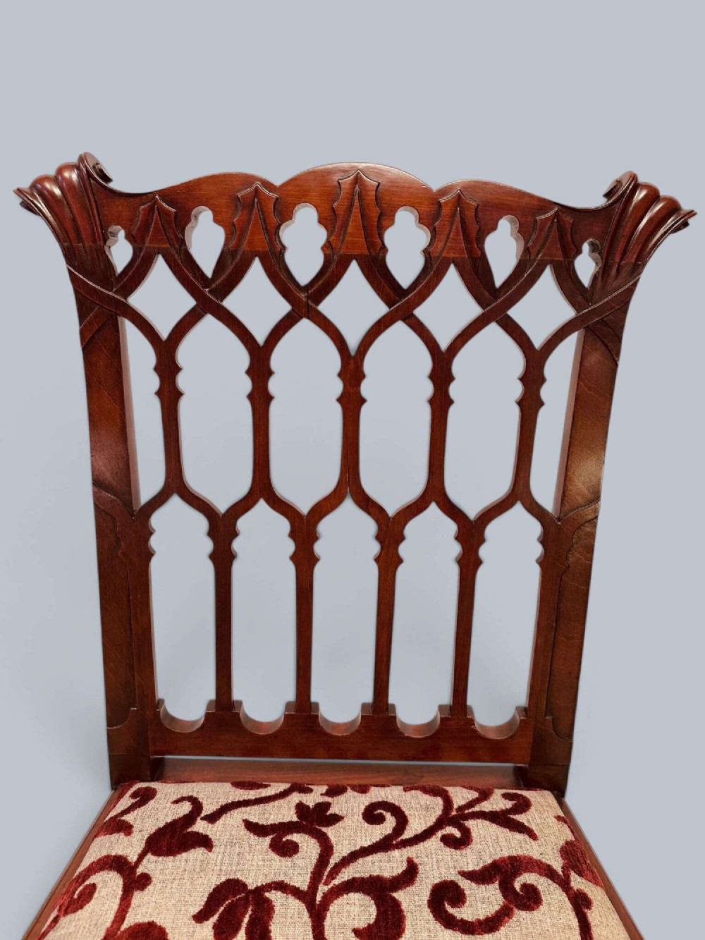 A pair of mahogany side chairs featuring pierced Gothic tracery backrests, straight square legs with H-stretchers, and patterned red fabric upholstery. View VIII