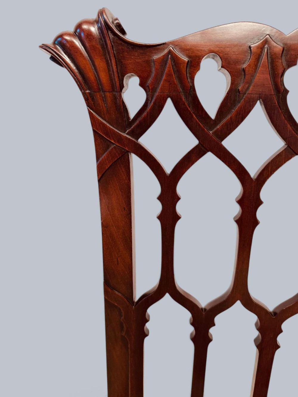 A pair of mahogany side chairs featuring pierced Gothic tracery backrests, straight square legs with H-stretchers, and patterned red fabric upholstery. View X