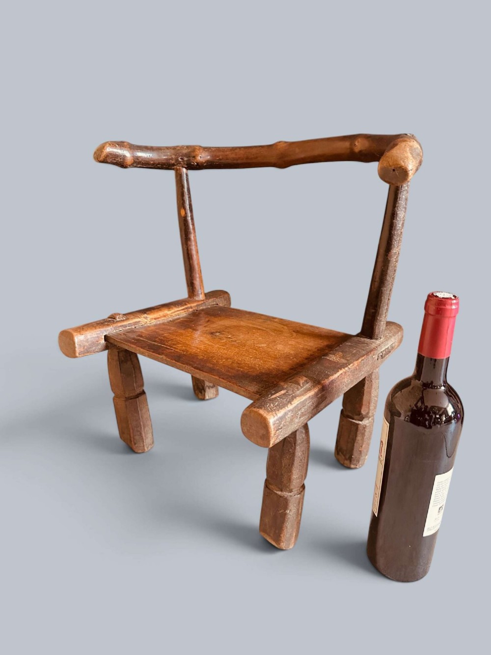 A small hand-carved rustic wooden child chair with a curved branch backrest and chunky square-cut legs.