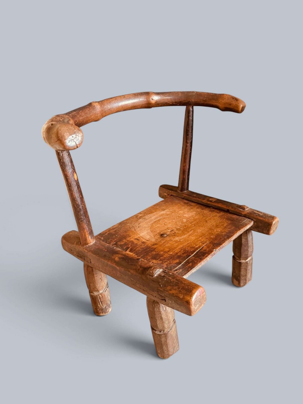 A small hand-carved rustic wooden child chair with a curved branch backrest and chunky square-cut legs. View II