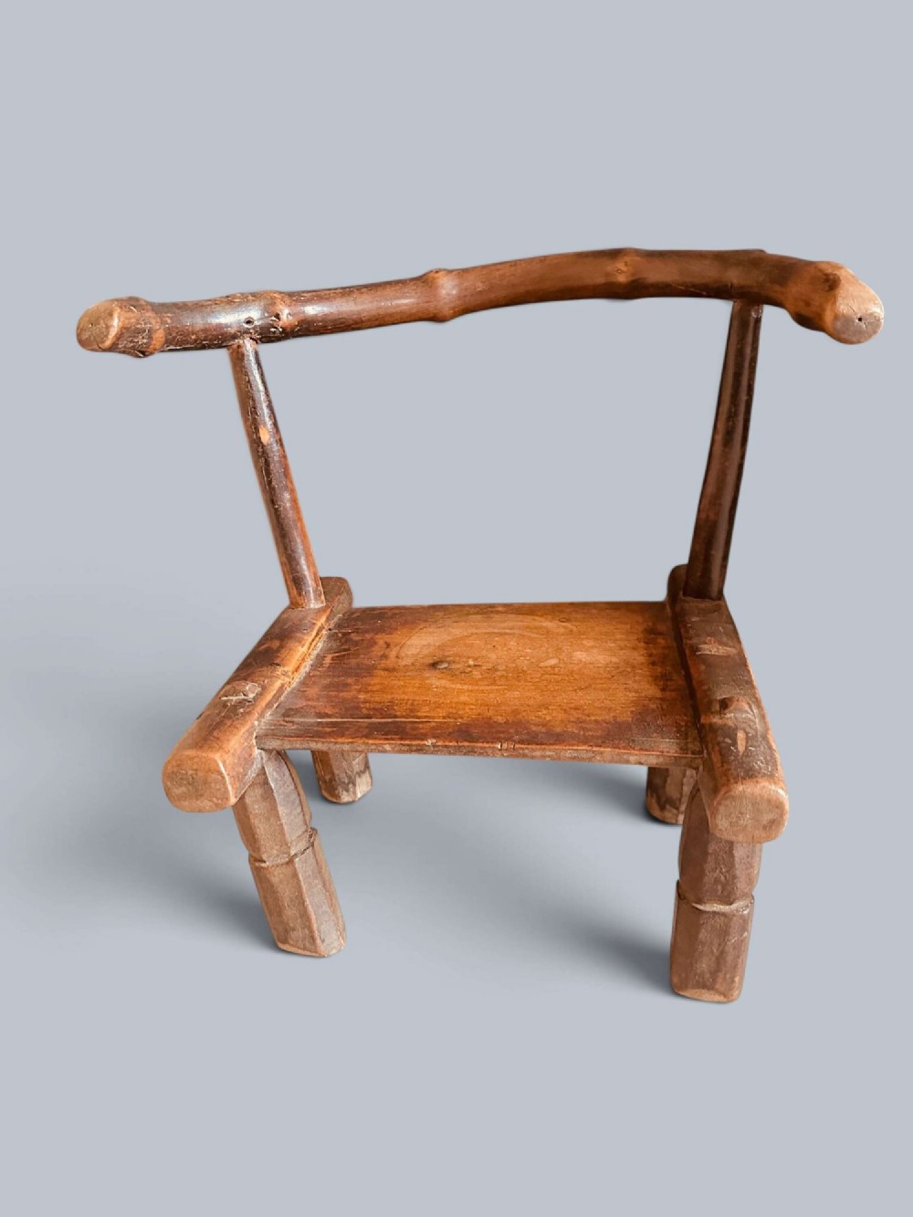 A small hand-carved rustic wooden child chair with a curved branch backrest and chunky square-cut legs. View III