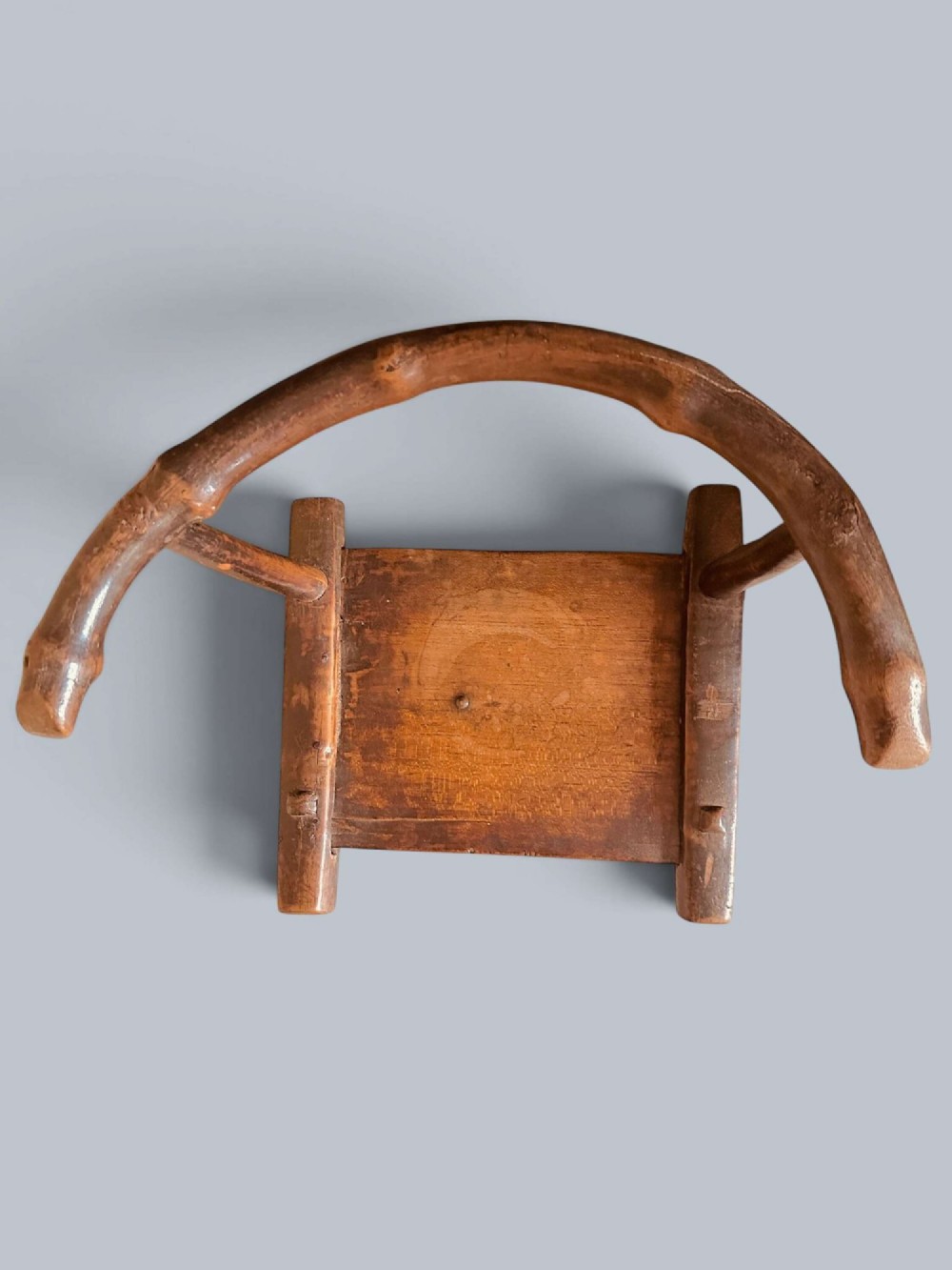 A small hand-carved rustic wooden child chair with a curved branch backrest and chunky square-cut legs. View X