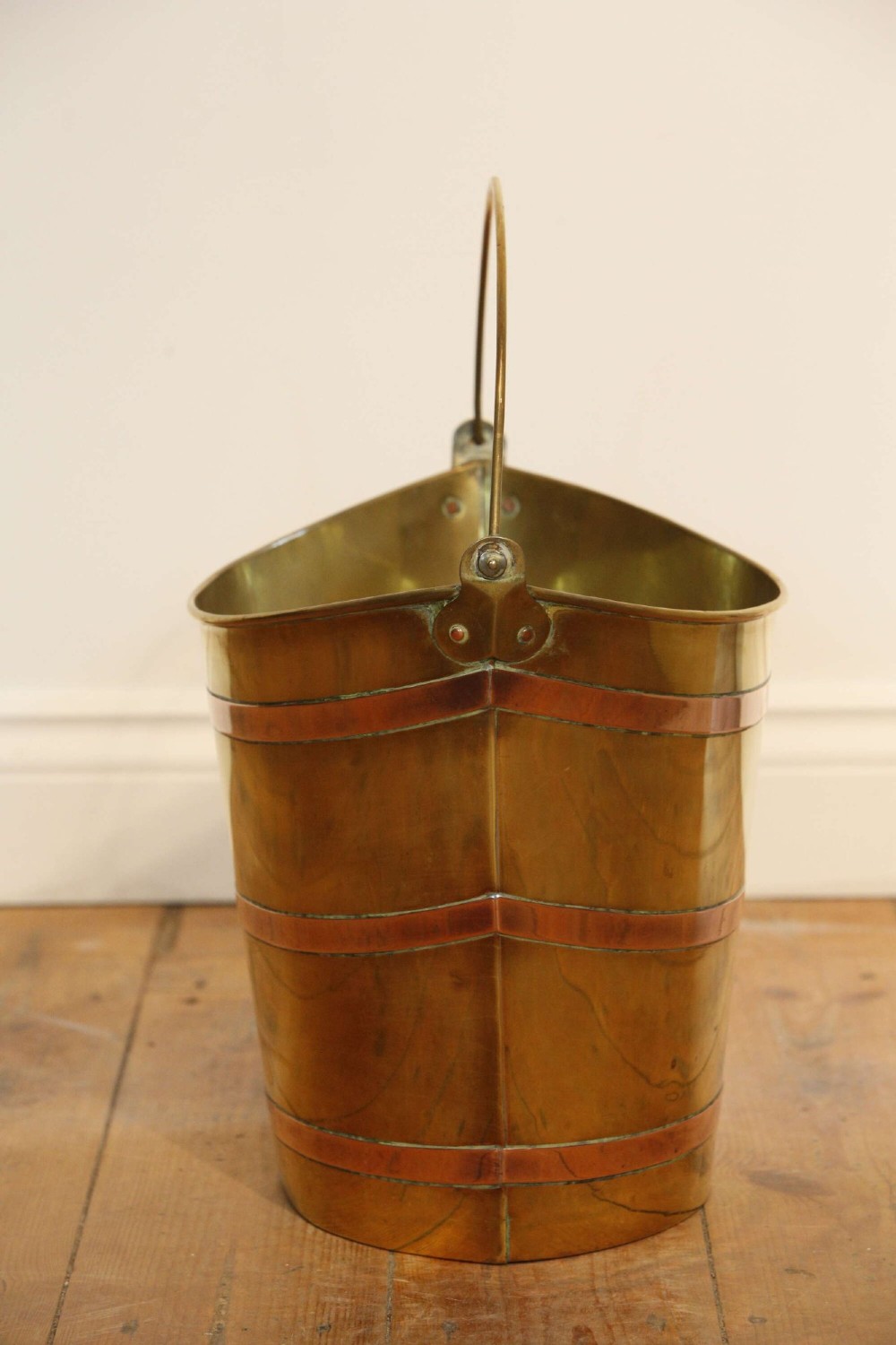 A Georgian brass peat bucket featuring flared sides, three horizontal copper bands, and a curved upper rim. View IX