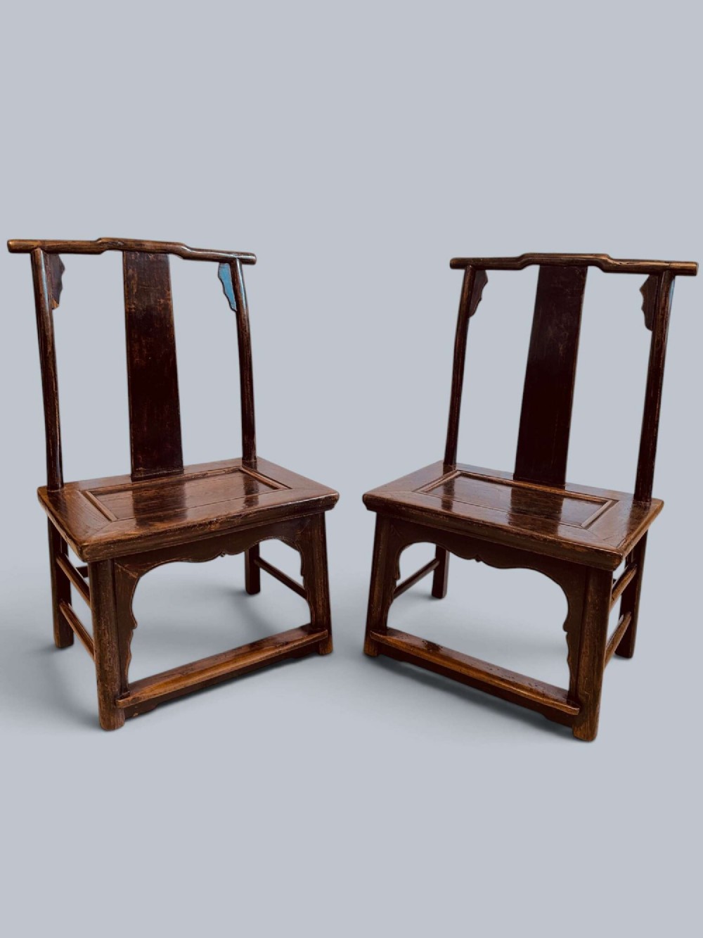 A pair of dark-lacquered antique Chinese childrens chairs with yoke-style top rails and carved aprons.
