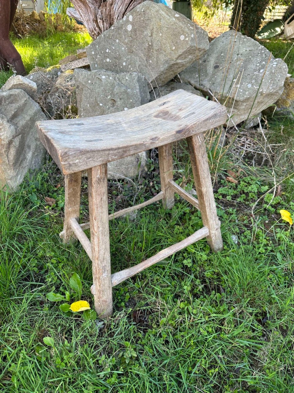 An antique weathered grey Chinese elm stool featuring a curved concave wooden seat, splayed legs, and exposed tenon joinery. View II