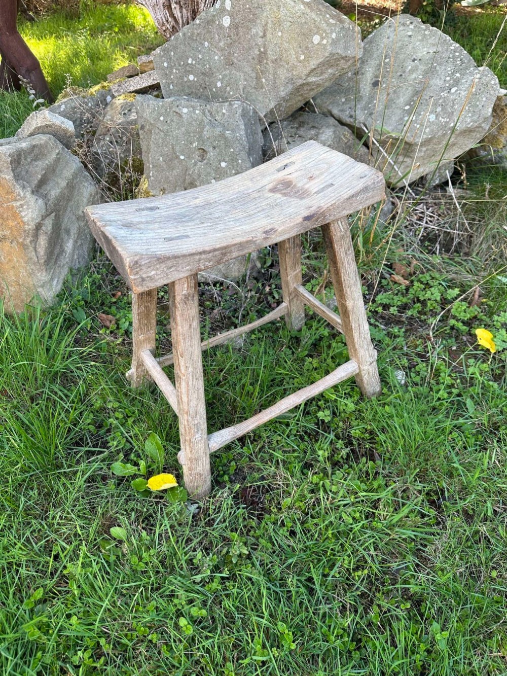 An antique weathered grey Chinese elm stool featuring a curved concave wooden seat, splayed legs, and exposed tenon joinery. View III