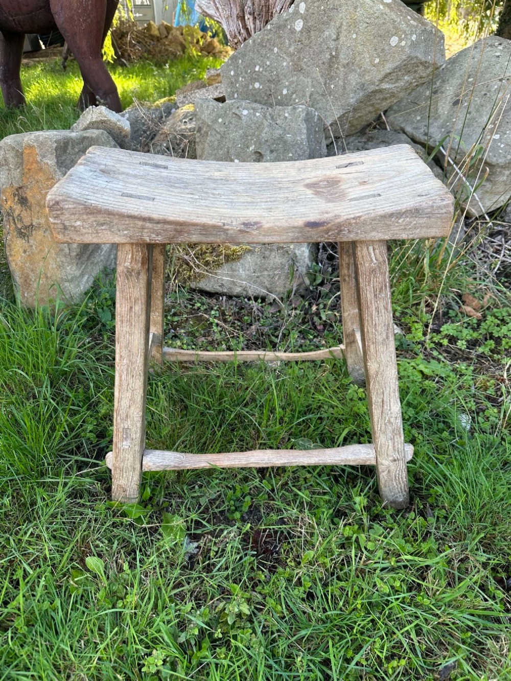 An antique weathered grey Chinese elm stool featuring a curved concave wooden seat, splayed legs, and exposed tenon joinery. View VII