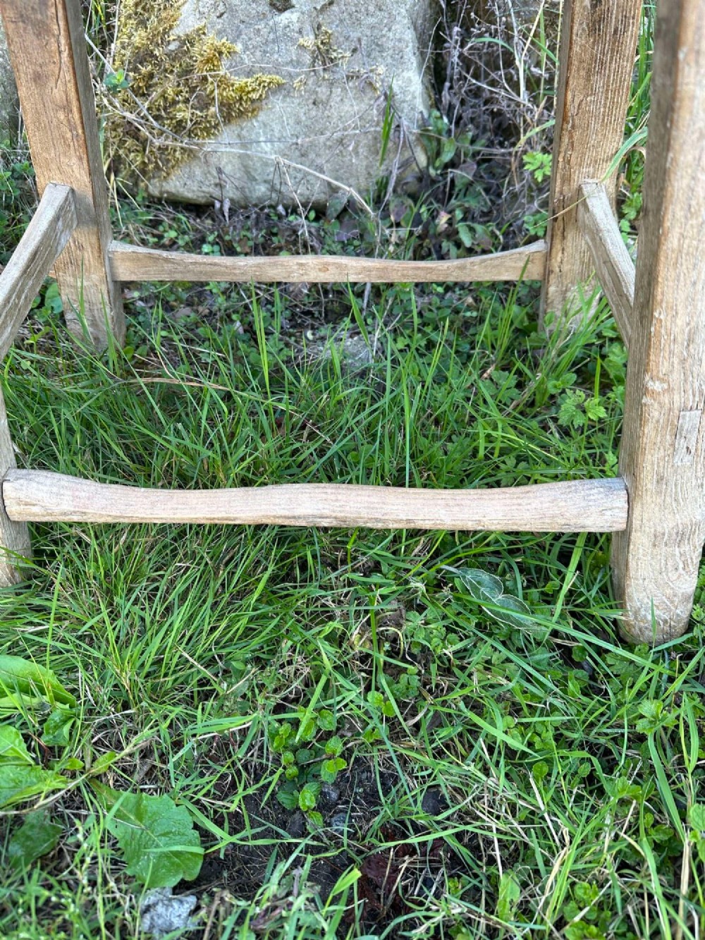 An antique weathered grey Chinese elm stool featuring a curved concave wooden seat, splayed legs, and exposed tenon joinery. View XI