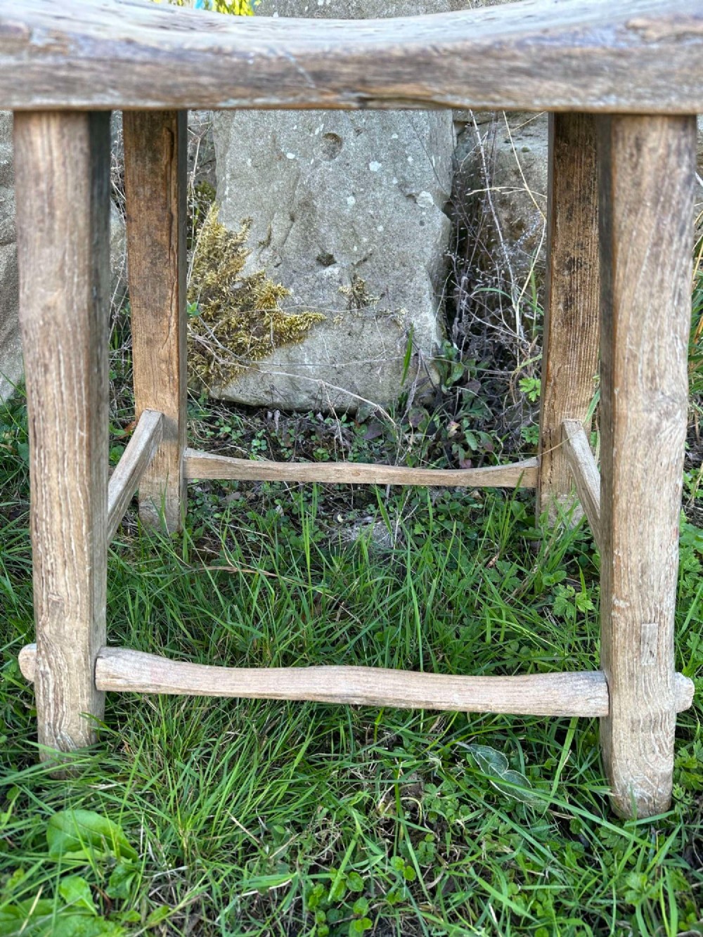 An antique weathered grey Chinese elm stool featuring a curved concave wooden seat, splayed legs, and exposed tenon joinery. View XII