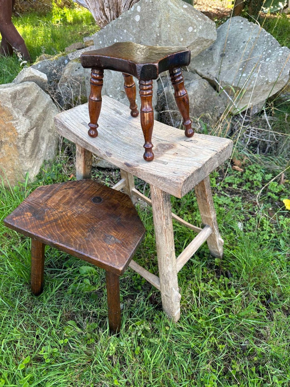 An antique weathered grey Chinese elm stool featuring a curved concave wooden seat, splayed legs, and exposed tenon joinery. View XIII