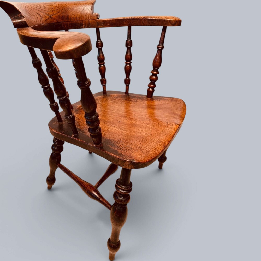 A near pair of warm brown antique elm Windsor captains chairs with turned spindles and curved armrests. View V