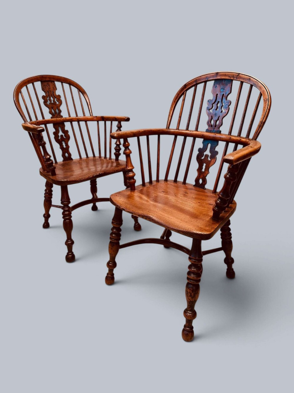 A pair of 19th-century yew wood Windsor armchairs featuring low hoop backs, pierced central splats, turned spindle supports, and shaped seats.