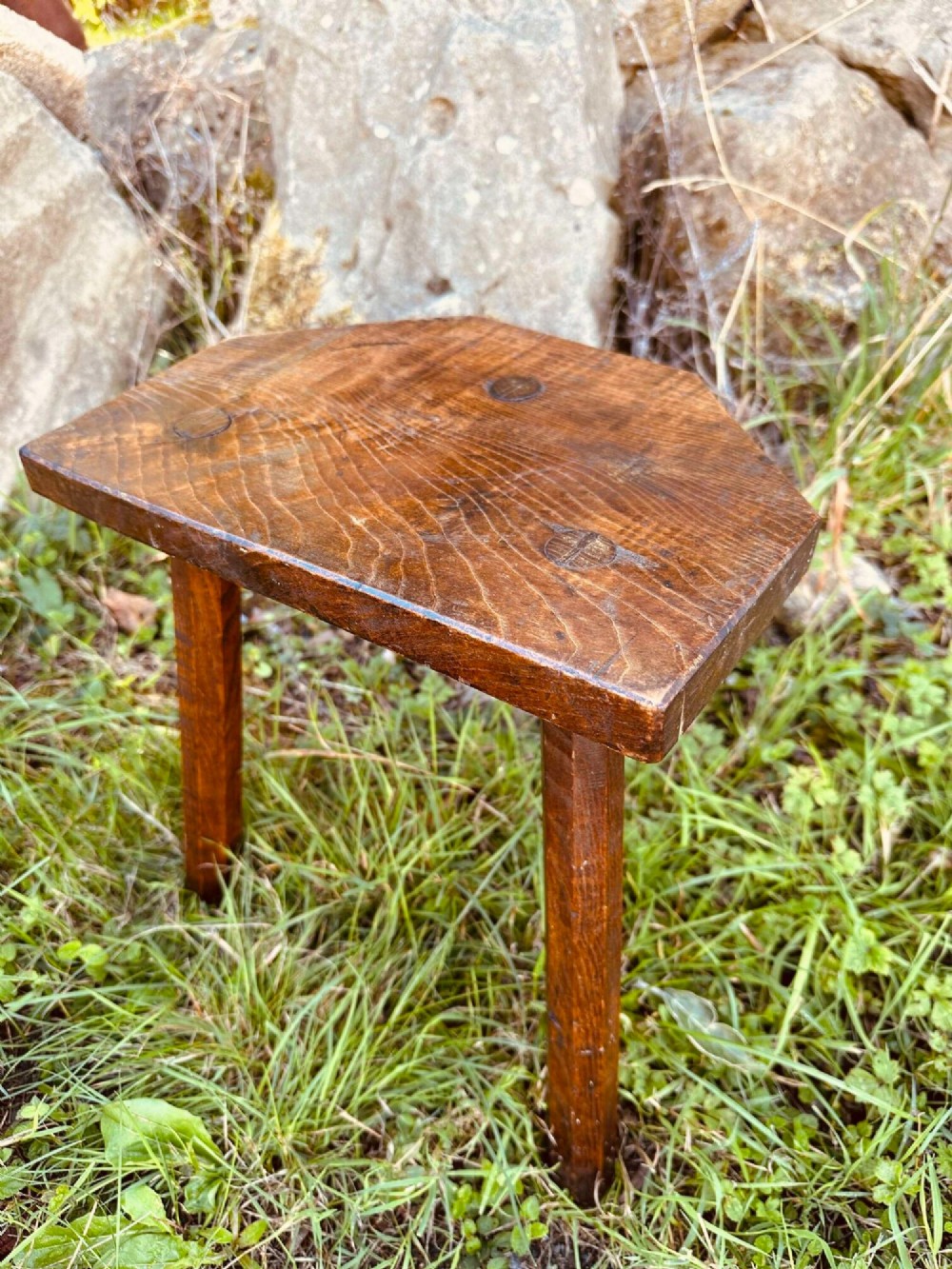 A rustic nineteenth-century three-legged wooden stool with a shaped elm seat and wedged tenon joinery visible on the top.