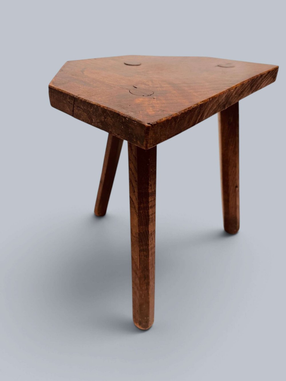 A rustic nineteenth-century three-legged wooden stool with a shaped elm seat and wedged tenon joinery visible on the top. View III