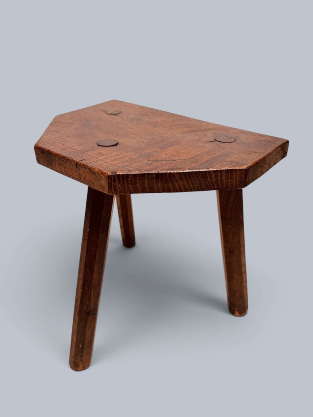 A rustic nineteenth-century three-legged wooden stool with a shaped elm seat and wedged tenon joinery visible on the top. View IV