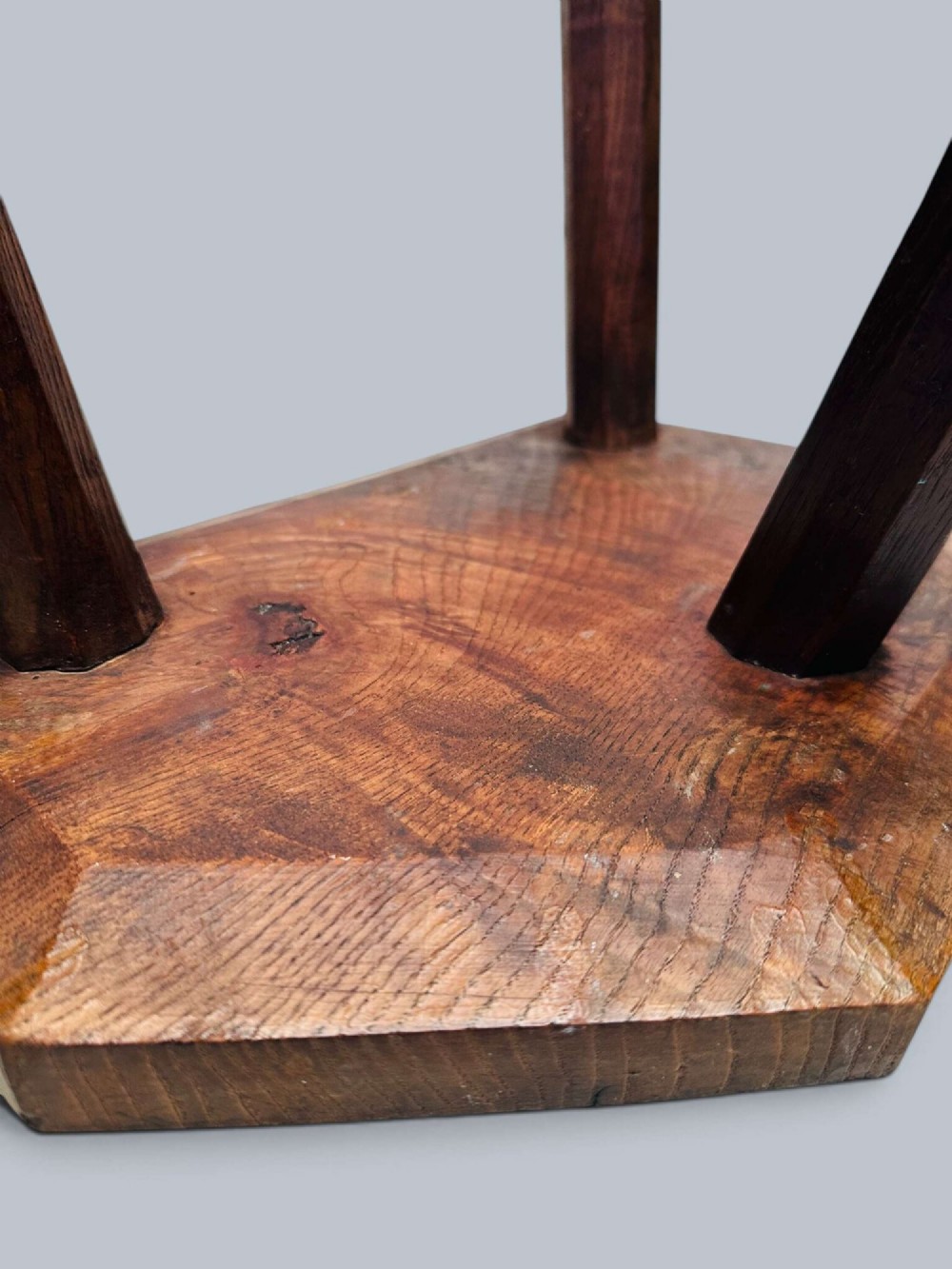 A rustic nineteenth-century three-legged wooden stool with a shaped elm seat and wedged tenon joinery visible on the top. View V