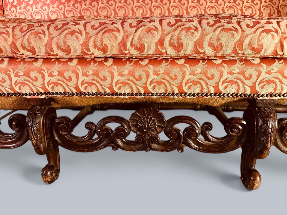 Late 19th-century Louis XIV style walnut sofa with intricately carved stretchers and red patterned damask fabric. View X
