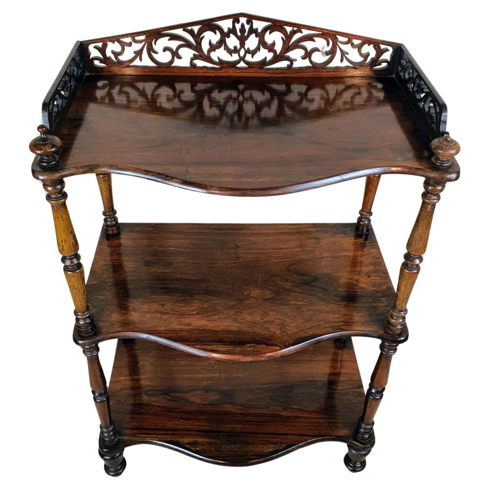 A three-tiered Victorian rosewood whatnot featuring turned spindle supports, serpentine-fronted shelves, and a decorative pierced fretwork top gallery.