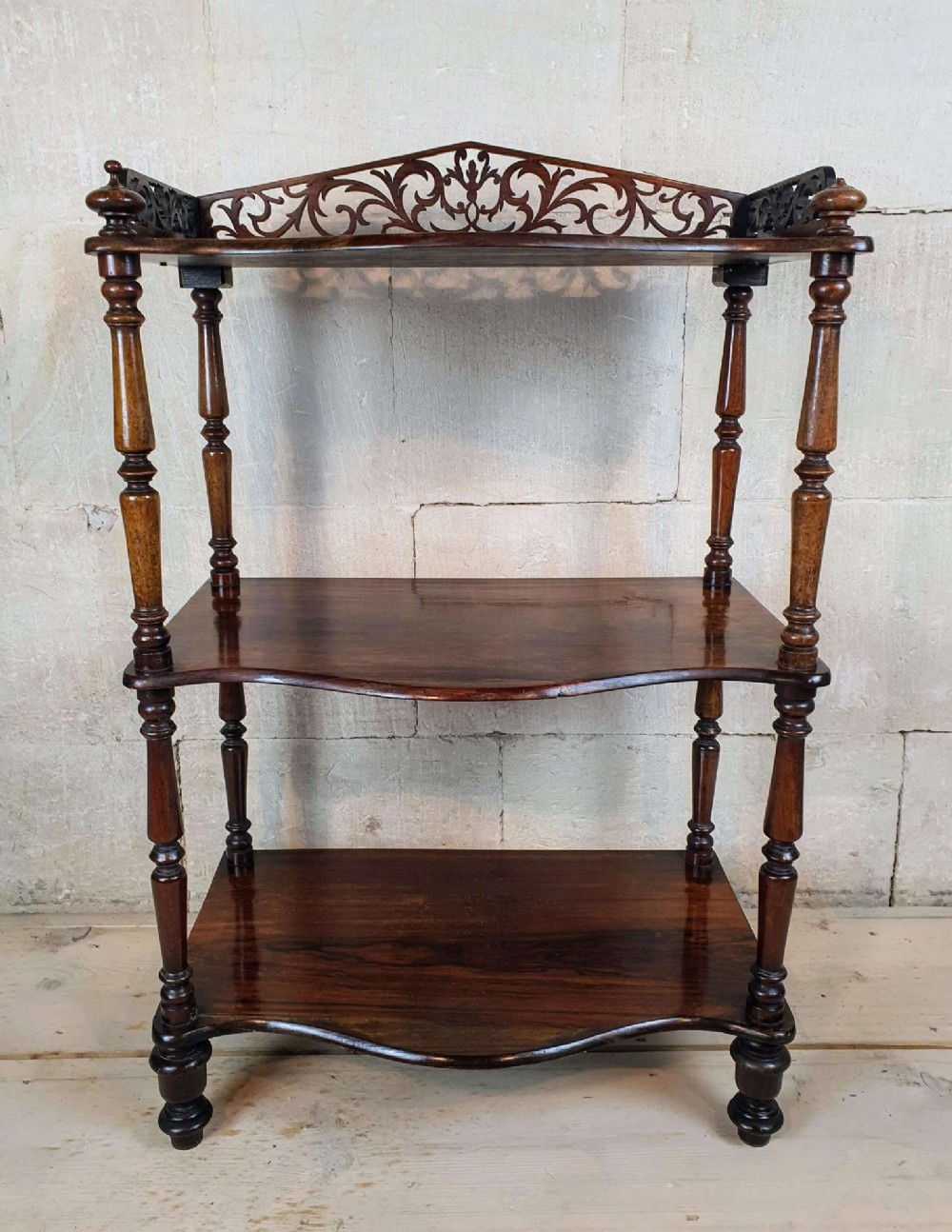 A three-tiered Victorian rosewood whatnot featuring turned spindle supports, serpentine-fronted shelves, and a decorative pierced fretwork top gallery. View II