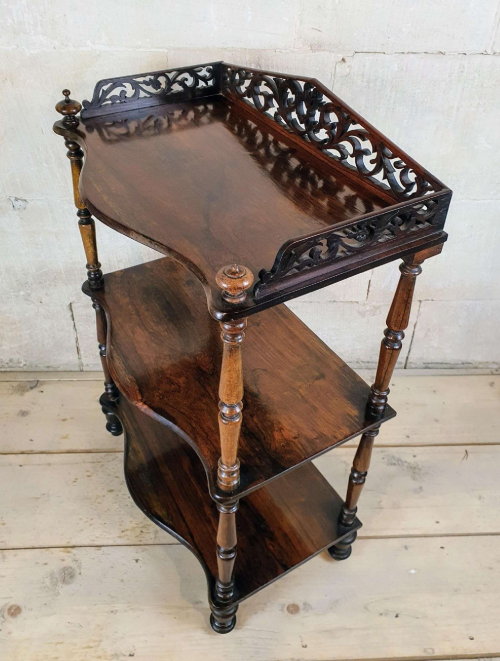 A three-tiered Victorian rosewood whatnot featuring turned spindle supports, serpentine-fronted shelves, and a decorative pierced fretwork top gallery. View IV
