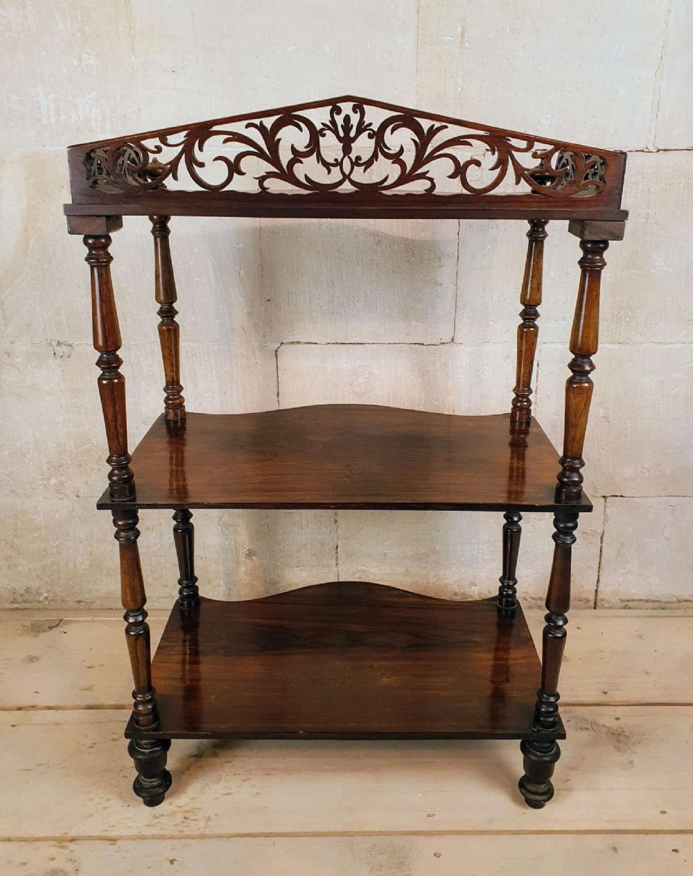 A three-tiered Victorian rosewood whatnot featuring turned spindle supports, serpentine-fronted shelves, and a decorative pierced fretwork top gallery. View V
