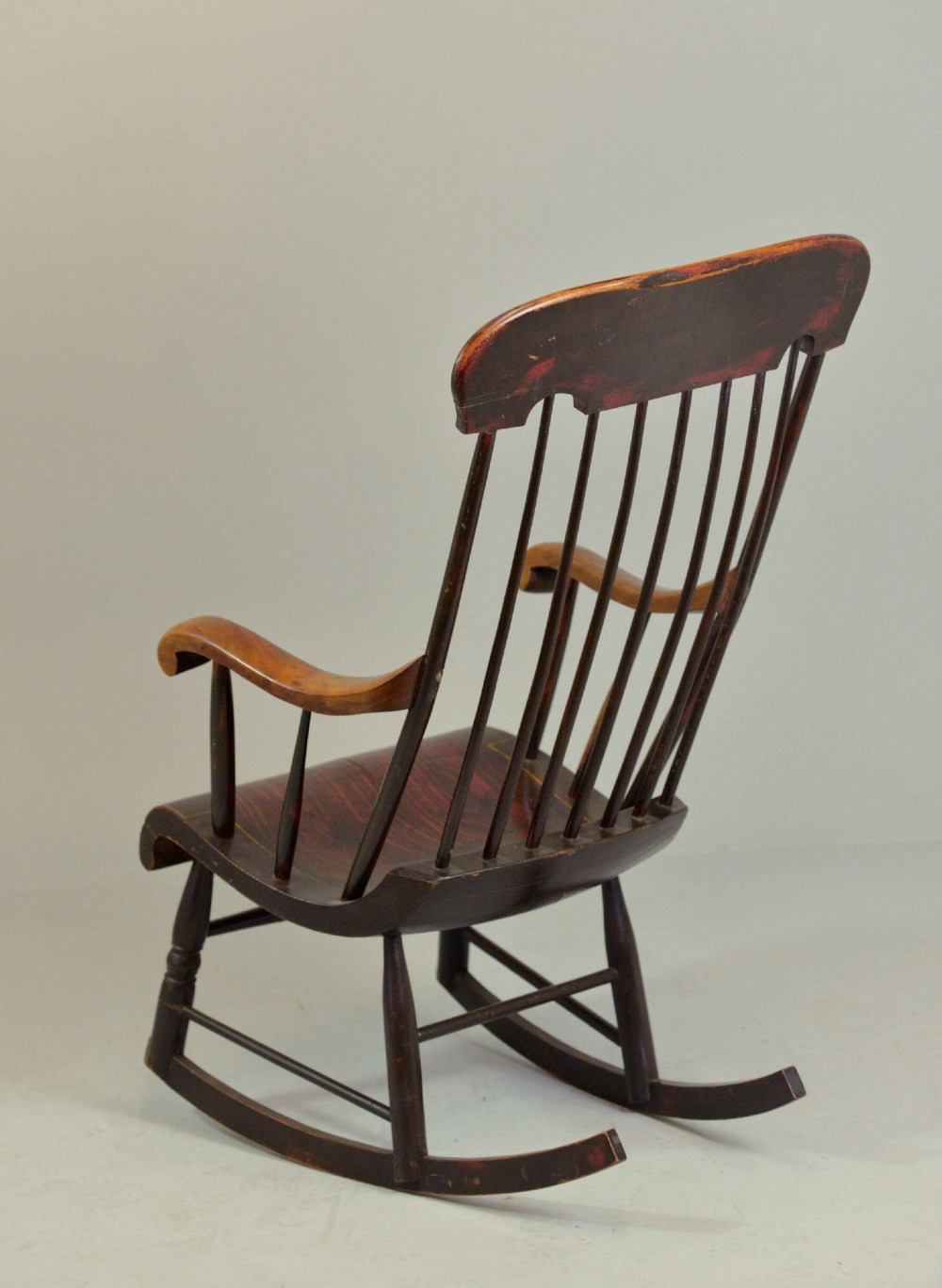 An antique American Boston rocking chair crafted from dark painted timber with a tall spindle back, scrolled arms, a sculpted seat, and a painted landscape motif across the top crest. View III