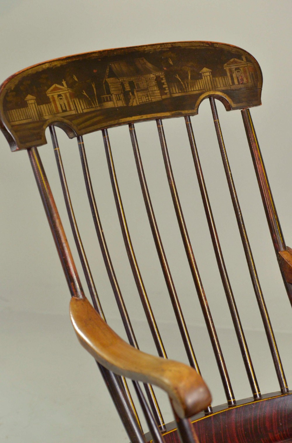 An antique American Boston rocking chair crafted from dark painted timber with a tall spindle back, scrolled arms, a sculpted seat, and a painted landscape motif across the top crest. View IV
