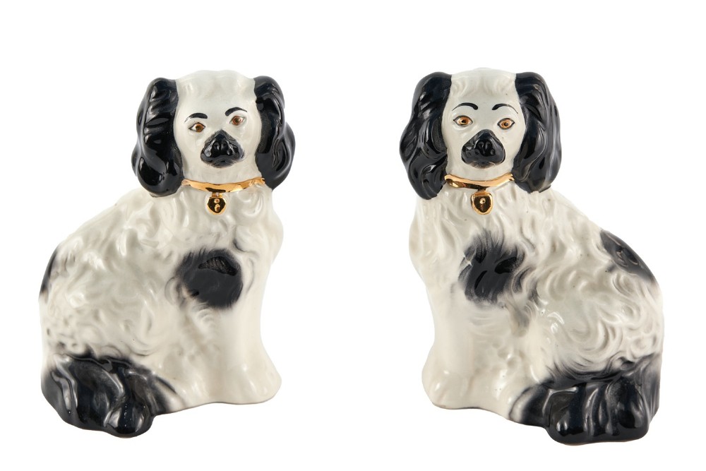 A pair of facing glazed white earthenware spaniel figurines with black patches and painted gilded collars.