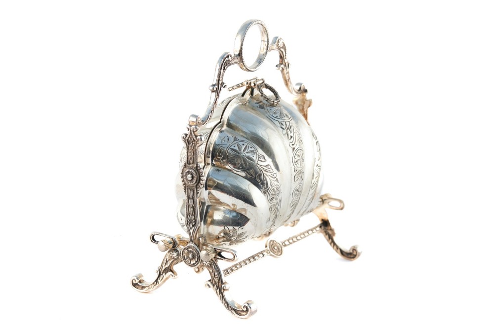 A Victorian silver-plated folding biscuit box in the form of a shell, decorated with engraved leaf motifs and supported by a cast metal stand.
